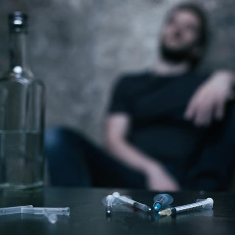 Blurred person in background with alcohol and drugs in foreground