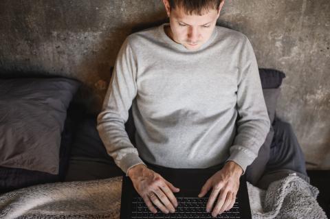 Man sitting on bed typing on keyboard