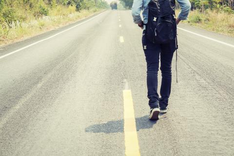 Person with backpack walking along bitumen road