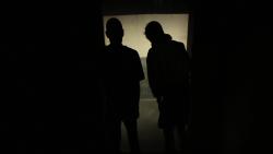 Two people standing in darkened room looking outside