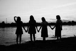 Silhouette of four women holding hands while standing on a beach