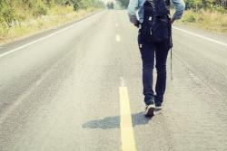 Person with backpack walking along bitumen road