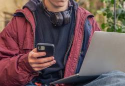 Person sitting down working on laptop with mobile phone in hand