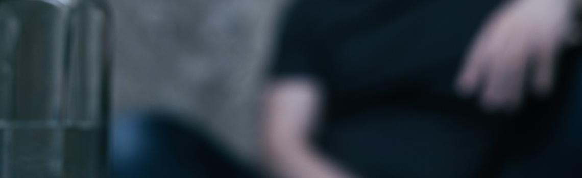 Blurred person in background with alcohol and drugs in foreground