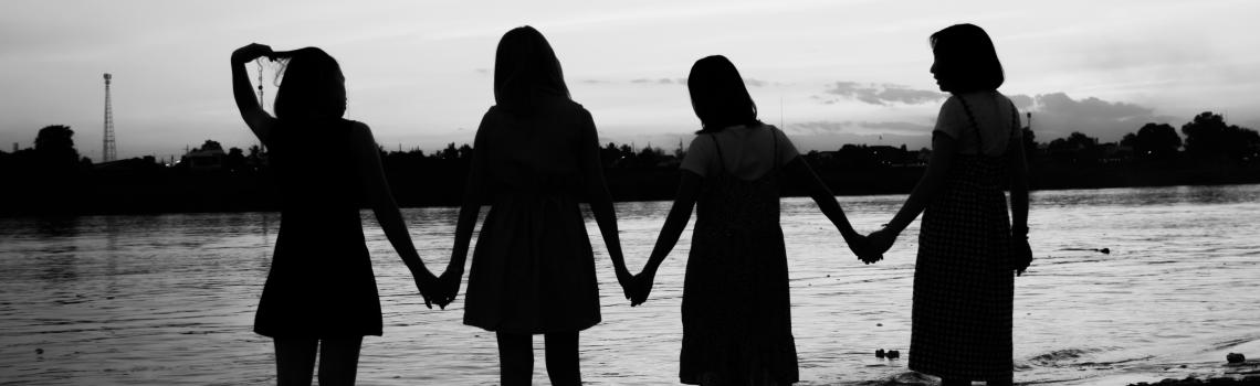 Silhouette of four women holding hands while standing on a beach
