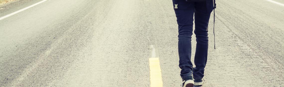 Person with backpack walking along bitumen road