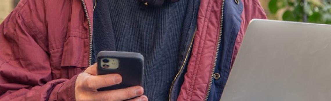 Person sitting down working on laptop with mobile phone in hand